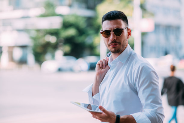 一个年轻的经纪人在高峰时间站在繁忙的街道旁看着他的平板电脑图片下载