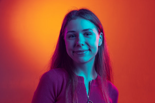 近距离年轻美丽的女孩看着相机和微笑孤立在橙色的背景霓虹灯，滤镜。情感的概念图片下载