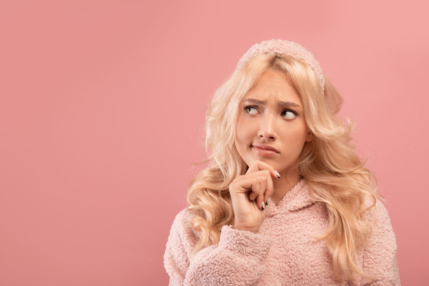 做出选择。沉思的年轻女士摸着下巴，看着一边的空间，想着什么，粉红色的背景图片下载