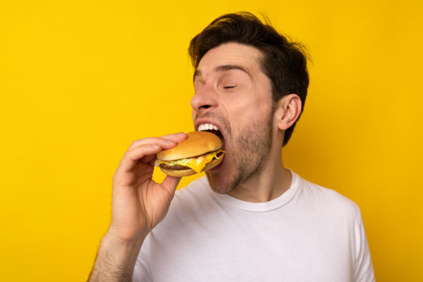 有趣的饥饿的家伙拿着汉堡，在工作室里咬三明治图片下载