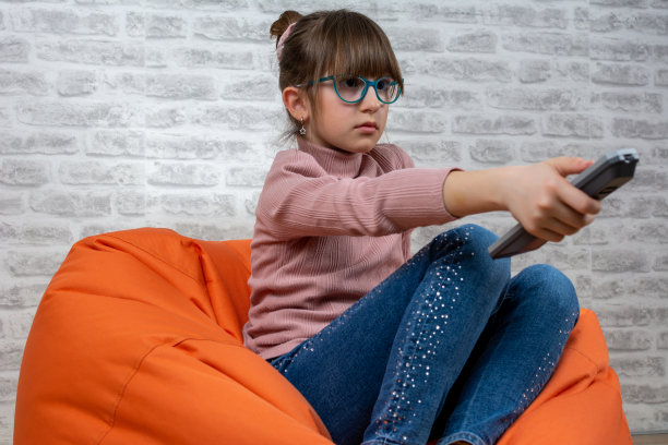 一个年轻的白人女孩坐在地板上看电视的前视图。图片下载