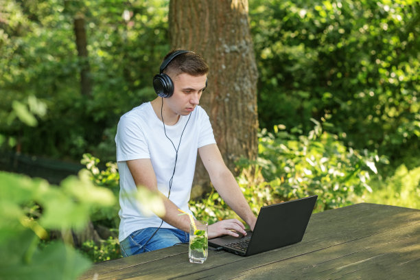 受自然启发的人。使用互联网、笔记本电脑和耳机进行远程工作和学习。配以薄荷和柠檬的美味清爽的鸡尾酒图片下载