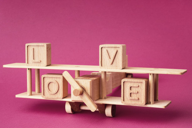 木制的儿童飞机和由粉红色背景上的立方体组成的单词爱。创意情人节，婚礼之旅，浪漫之旅。明亮的明信片，爱情的背景图片下载