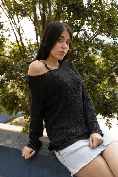 女模特摆姿势放松地坐在一个被大自然包围的公园里，穿着休闲的黑色甜美和裙子，生活方式图片下载