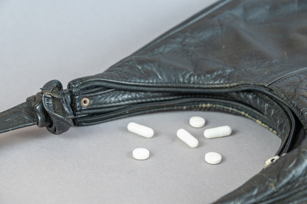 灰色背景下，一个黑人老太太的手提包和一些药品。一件女人的皮衣配件里洒出了各种麦卡乐氏药物。有选择性的重点图片下载