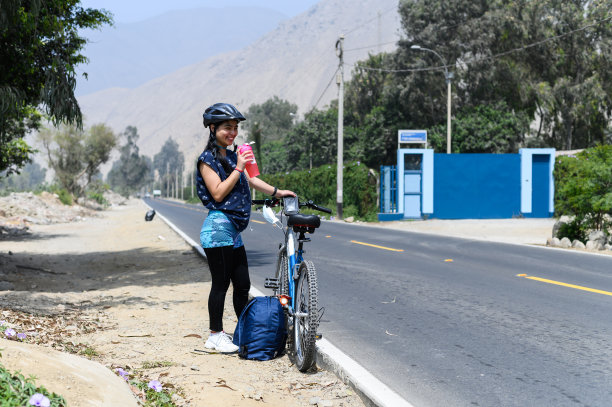 运动结束后，一名微笑的女子在自行车旁喝水。图片下载