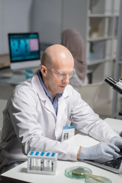 成熟男性，穿着白大褂，戴着防护手套和眼镜，在桌前打字图片下载