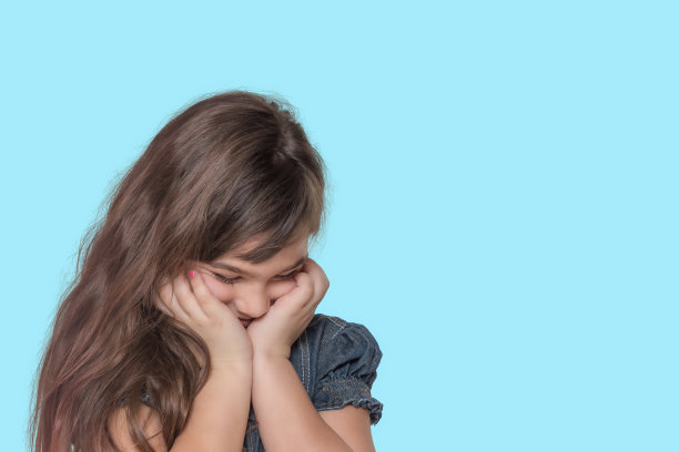 晒黑的羞愧的小女孩在青色的背景上摆姿势。图片下载