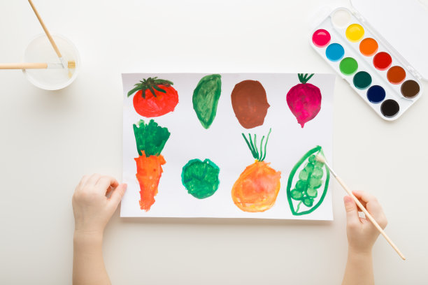 宝宝手拿画笔，在白纸上画出不同颜色的蔬菜形状。特写镜头。视角拍摄。幼儿的发展。自顶向下的观点。图片下载