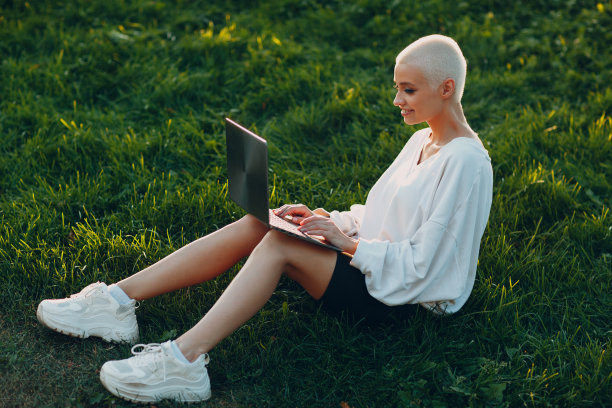 千禧一代的年轻女子金发短发户外微笑的肖像与笔记本电脑。图片下载