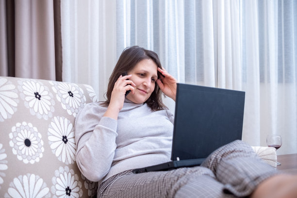 一名年轻女子在酒店房间里一边用电脑工作，一边拉直头发图片下载