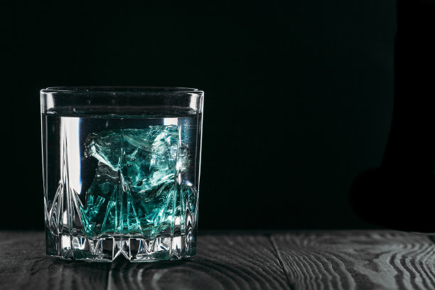 杜松子酒装在玻璃杯里，黑色背景，蓝色冰块放在木头表面。酒精与冰。铭文的地方。“n图片下载