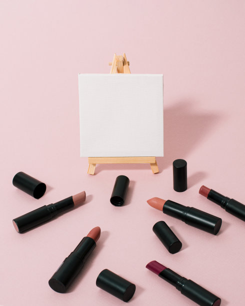 彩妆唇膏在木架上的空白油画画布上的蜡笔粉红色背景与复制空间。简约的艺术理念，选择合适的颜色。女人的美丽配件。图片下载