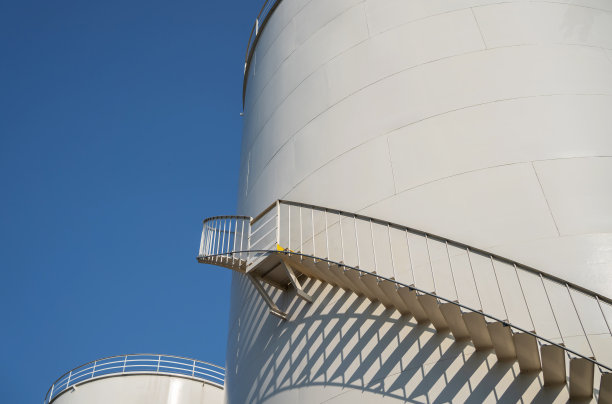 蓝天下的石油厂基础油储罐弧形楼梯。石油工业工厂。用于汽车发动机油和工业用油的基础油。图片下载