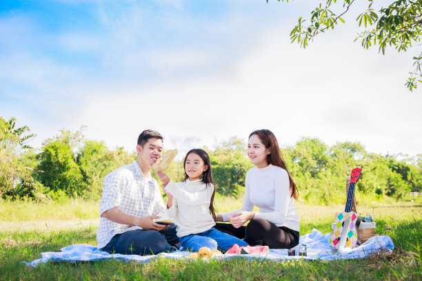 幸福的家庭野餐。亚洲父母(爸爸、妈妈)和女儿在阳光明媚的日子里，在绿色的花园里，在野餐布上野餐，玩着玩具飞机，玩得很开心图片下载