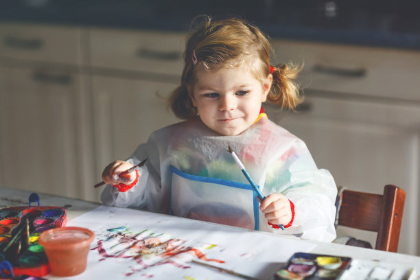 可爱的小女孩学习用水彩画。蹒跚学步的小孩在家里用彩色笔刷画画。健康快乐的女儿在家里或托儿所尝试颜色，水图片下载
