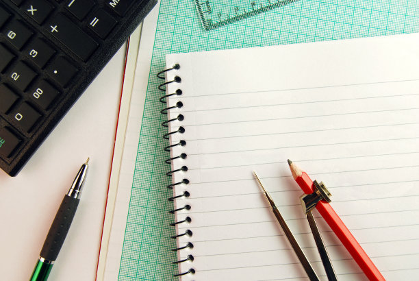 几何工具——一个打开的指南针放在一张螺旋形记事本和画纸上，后面还有计算器和方框。图片下载