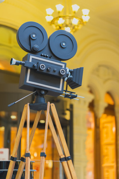 老式电影相机在三脚架上，模型，在抽象的金色背景上。电影和古物概念。图片下载