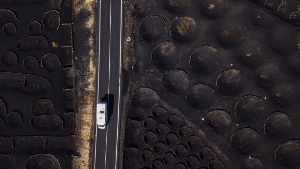 白色的露营车旅行和驾驶在一个长直的道路在风景优美的火山地区。以上无人机鸟瞰图的人和旅游概念。从垂直角度看，黑砂火山地面图片下载