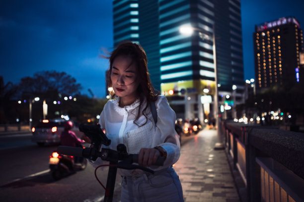 亚洲中国女人在城市里骑电动车，用智能手机图片下载