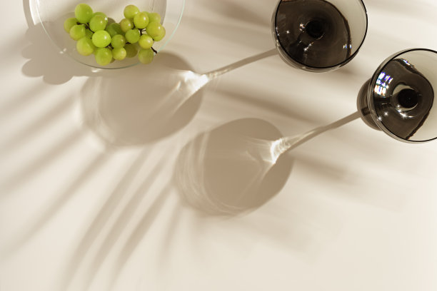 香槟玻璃着色灰色玻璃和葡萄米色背景与棕榈叶阴影，从太阳眩光。最小的夏季休息概念。用彩色玻璃器皿装的汽酒。创造性的俯视图图片下载