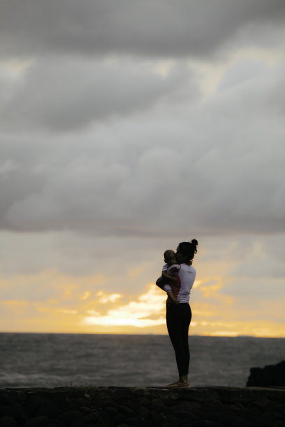 夕阳下，母亲抱着小男孩在海滩上图片下载