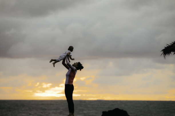 夕阳下，母亲抱着小男孩在海滩上图片下载