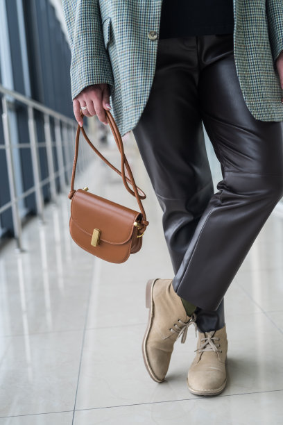 女孩穿着黑色皮裤，别致的夹克和经典的鞋子，一个时髦的棕色手提包图片下载