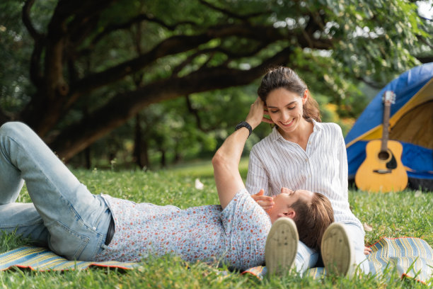 年轻的情侣躺在草地上，感觉很浪漫。爱情和温柔，浪漫的男人对他的女朋友微笑，生活方式的概念图片下载