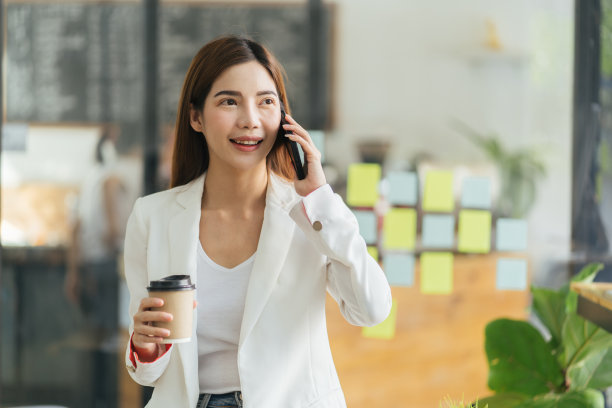 办公室生活方式，商业和人的概念。有吸引力的年轻亚洲女子检查她的手机短信，喝外卖咖啡，看着智能手机显示满意的微笑，在聊天短信。图片下载