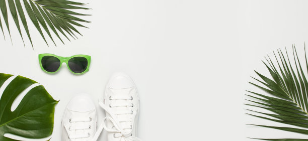 白色的女性时尚运动鞋，时髦的太阳镜，浅灰色的背景上的热带树叶。平躺顶视图复制空间。女性的鞋子,配饰。时尚的白色运动鞋。夏天创意概念图片下载