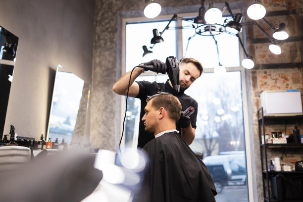 理发师在理发店用发胶和梳子给头发定型。年轻英俊的白人男子在一个现代发廊理发图片下载