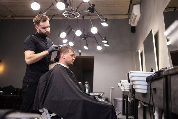 理发师在理发店用发胶和梳子给头发定型。年轻英俊的白人男子在一个现代发廊理发图片下载
