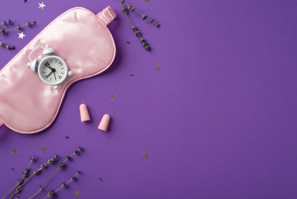 俯视图照片大丝绸眼罩与一个小的白色时钟上，两个粉红色的耳塞和分散的五彩纸屑在紫色孤立的背景copyspace的星星形状图片下载
