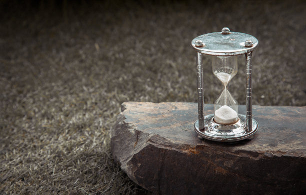 银色沙漏或沙漏在草地背景上巨大的石头。图片下载