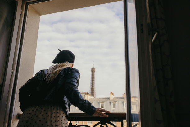 在巴黎，一个成年女子倚在她酒店房间的窗外，俯视着街道，背景是埃菲尔铁塔图片下载