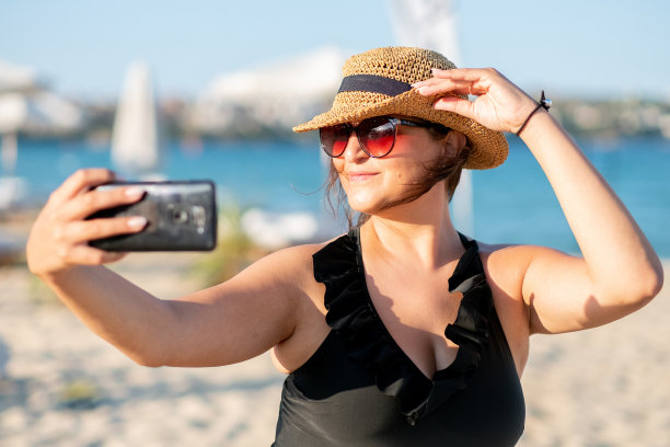 一名身穿黑色泳衣的年轻女子在海滩上自拍图片下载