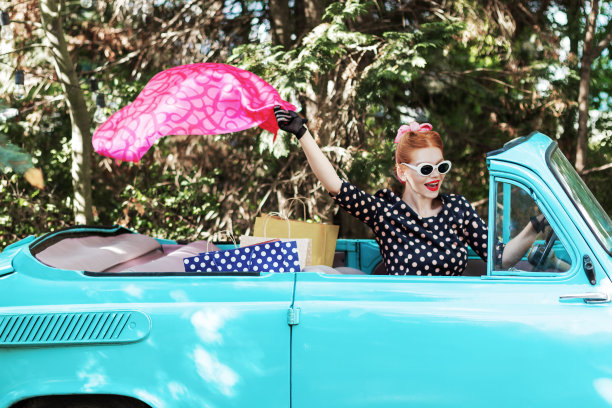 一个穿着复古衣服的女人在购物后开着一辆旧车。图片下载