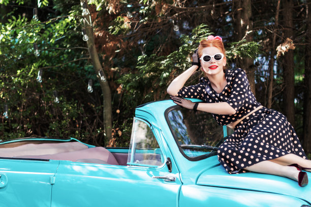 穿着复古衣服的海报女郎，坐在旧车上。图片下载