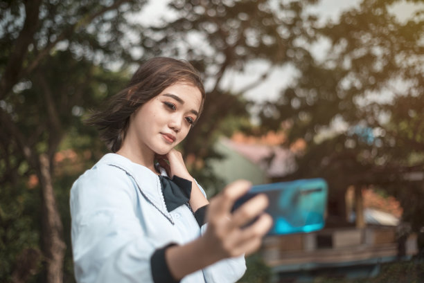 一个漂亮优雅的年轻亚洲女子穿着学生制服在公园里自拍。为社交媒体拍照。图片下载