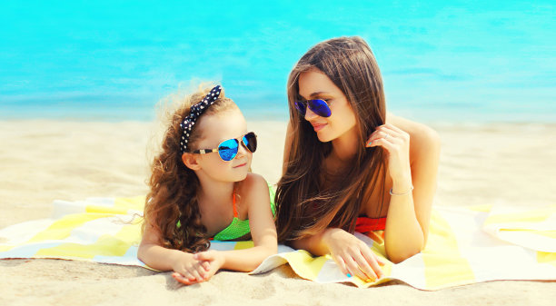 暑假的照片，母亲和孩子一起躺在沙滩上，背景是大海图片下载