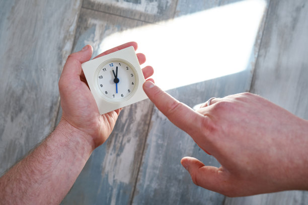 一个男人手里拿着一块白色的表。有复制空间的浅背景上的时钟图像。斯堪的纳维亚风格的房间。时钟和时间图片下载