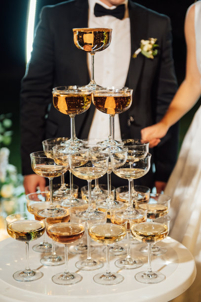 在晚上的仪式中，在拱门处的一个由香槟酒杯组成的大金字塔。新娘和新郎拥抱在一起图片下载