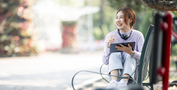 快乐年轻美丽的学生女孩坐在户外的自然公园使用笔记本电脑。图片下载