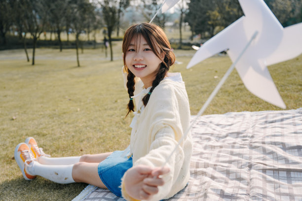 一个美丽的亚洲女孩坐在毯子上在一个阳光明媚的日子玩纸风车图片下载