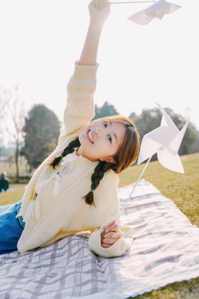 一个美丽的亚洲女孩坐在毯子上在一个阳光明媚的日子玩纸风车图片下载