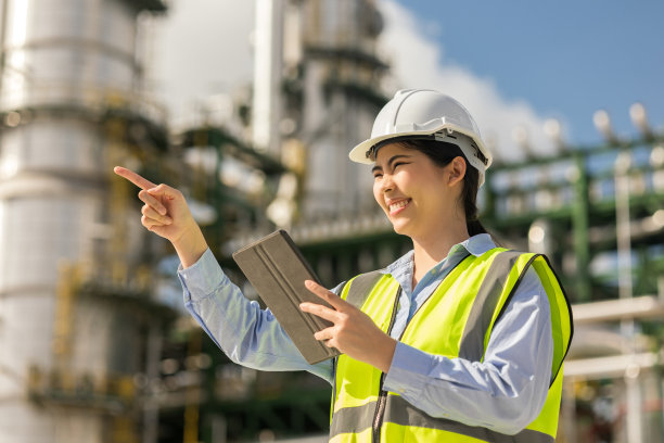 戴着白色安全帽的亚洲工程师经理站在炼油厂前。工业园区天然气石化。工厂储油罐及管道。炼油厂建设中的工人。图片下载