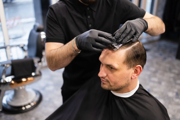 理发师在理发店用发胶和梳子给头发定型。年轻英俊的白人男子在一个现代发廊理发图片下载