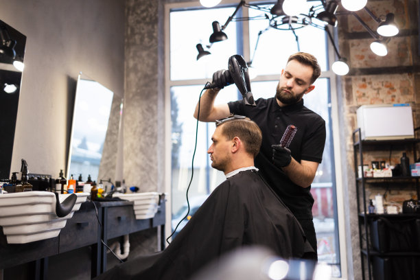 理发师在理发店用发胶和梳子给头发定型。年轻英俊的白人男子在一个现代发廊理发图片下载