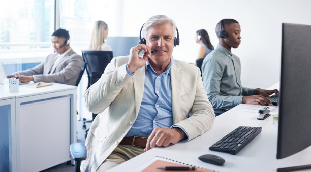 一个成熟的商人在现代办公室使用耳机和电脑的肖像图片下载